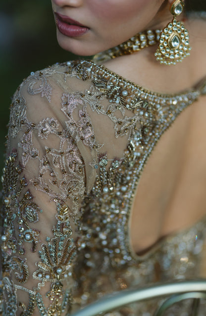 Close-up of a woman wearing an ornate embellished gold and silver beaded gown with intricate embroidery, pearl-like details, and a matching statement earring.