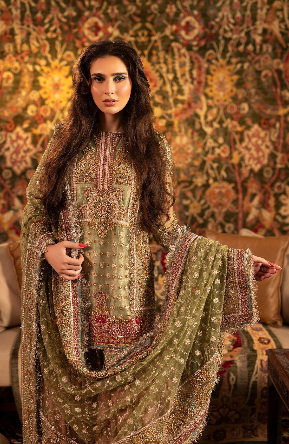 Woman in a traditional embroidered outfit with a floral-patterned wall in the background