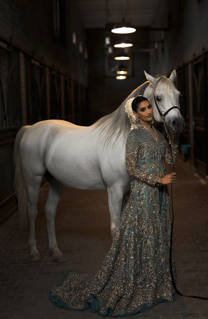 Woman in a floral dress standing next to a white horse in a stable.