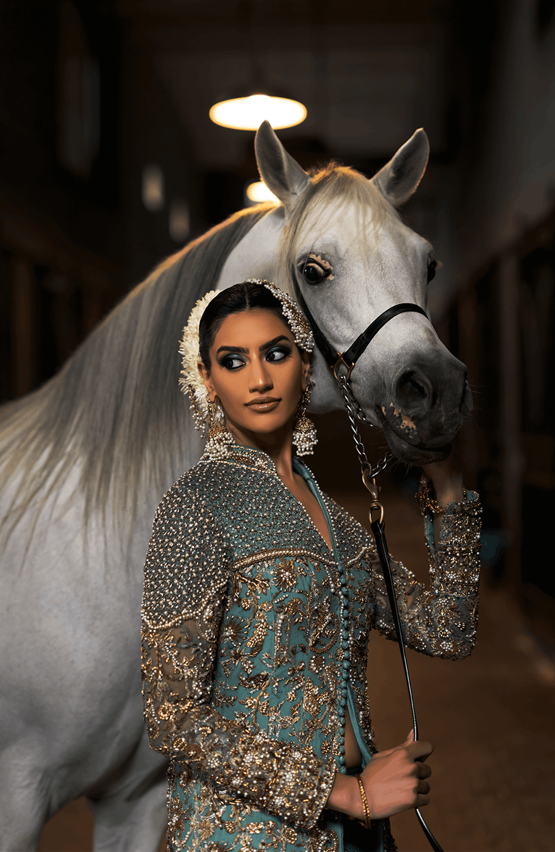 Woman in traditional attire standing next to a white horse indoors.
