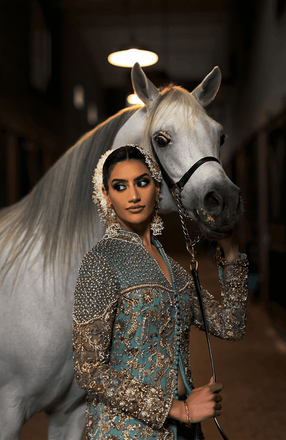 Woman in traditional attire standing next to a white horse indoors.