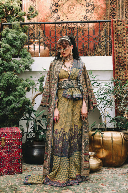 Woman in a patterned outfit standing in an ornate indoor setting with plants and decorative items.