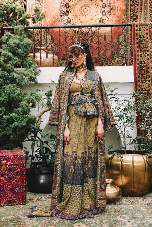 Woman in a patterned outfit standing in an ornate indoor setting with plants and decorative items.