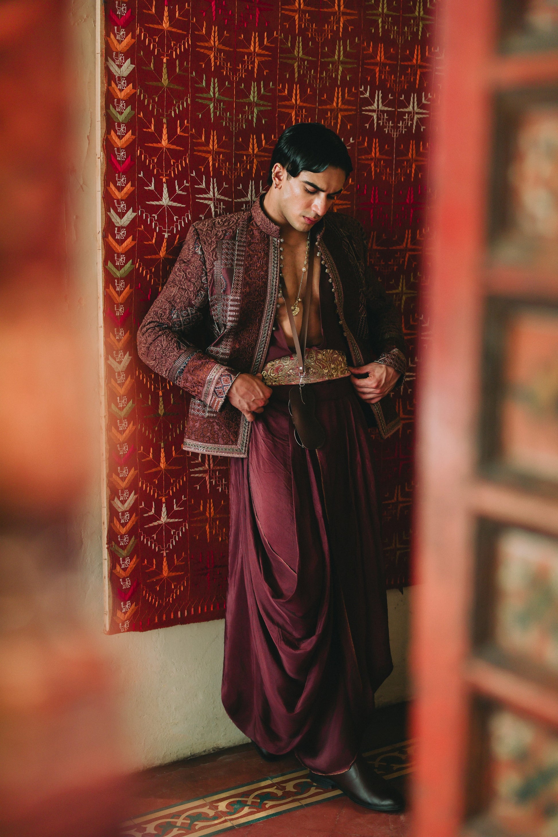 Person in traditional attire standing in a room with decorative walls.