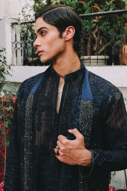 Person wearing a dark blue embroidered traditional outfit with a blurred background