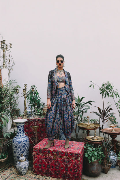 Woman in a patterned outfit standing in a room with plants and decorative items.