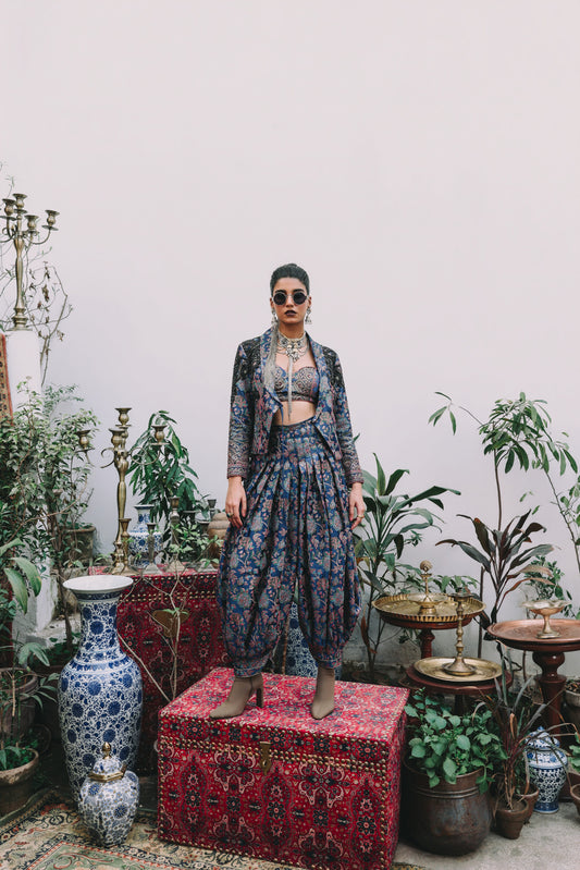 Woman in a patterned outfit standing in a room with plants and decorative items.