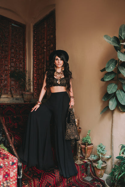 Woman in a black outfit standing in a room with plants and patterned rug.