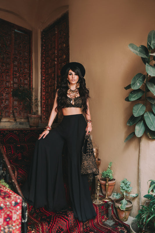 Woman in a black outfit standing in a room with plants and patterned rug.