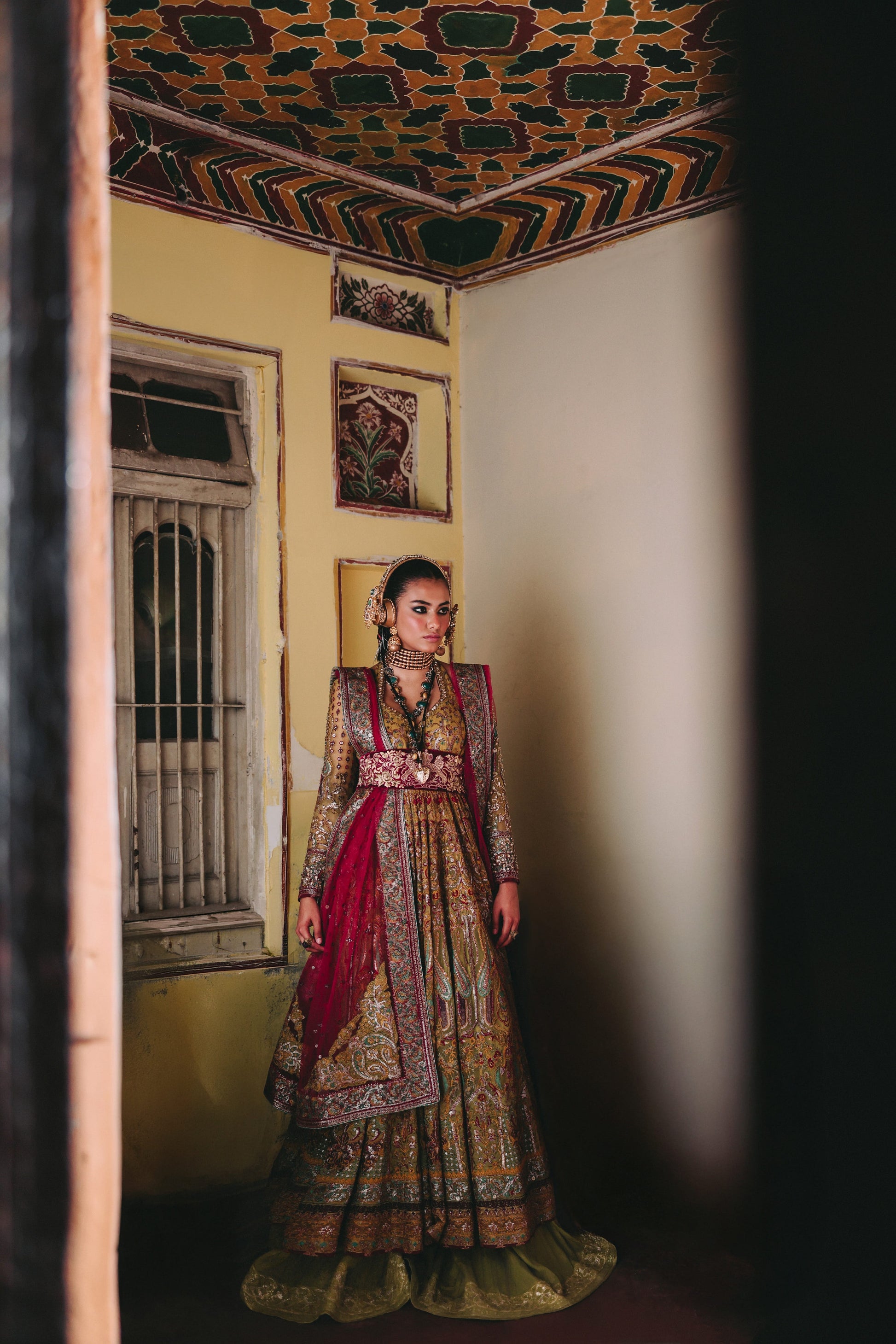 Woman in traditional attire standing in a room with decorative ceiling and walls.