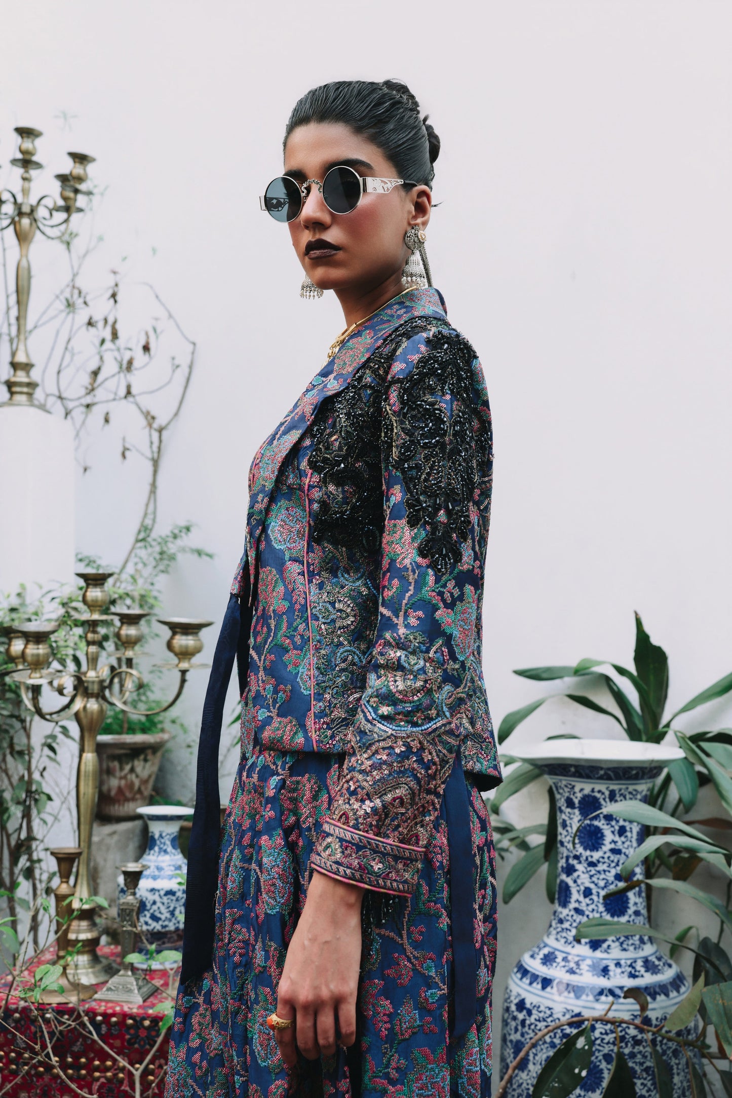 Woman in a patterned outfit standing in an elegant interior setting with decorative elements.