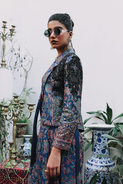 Woman in a patterned outfit standing in an elegant interior setting with decorative elements.