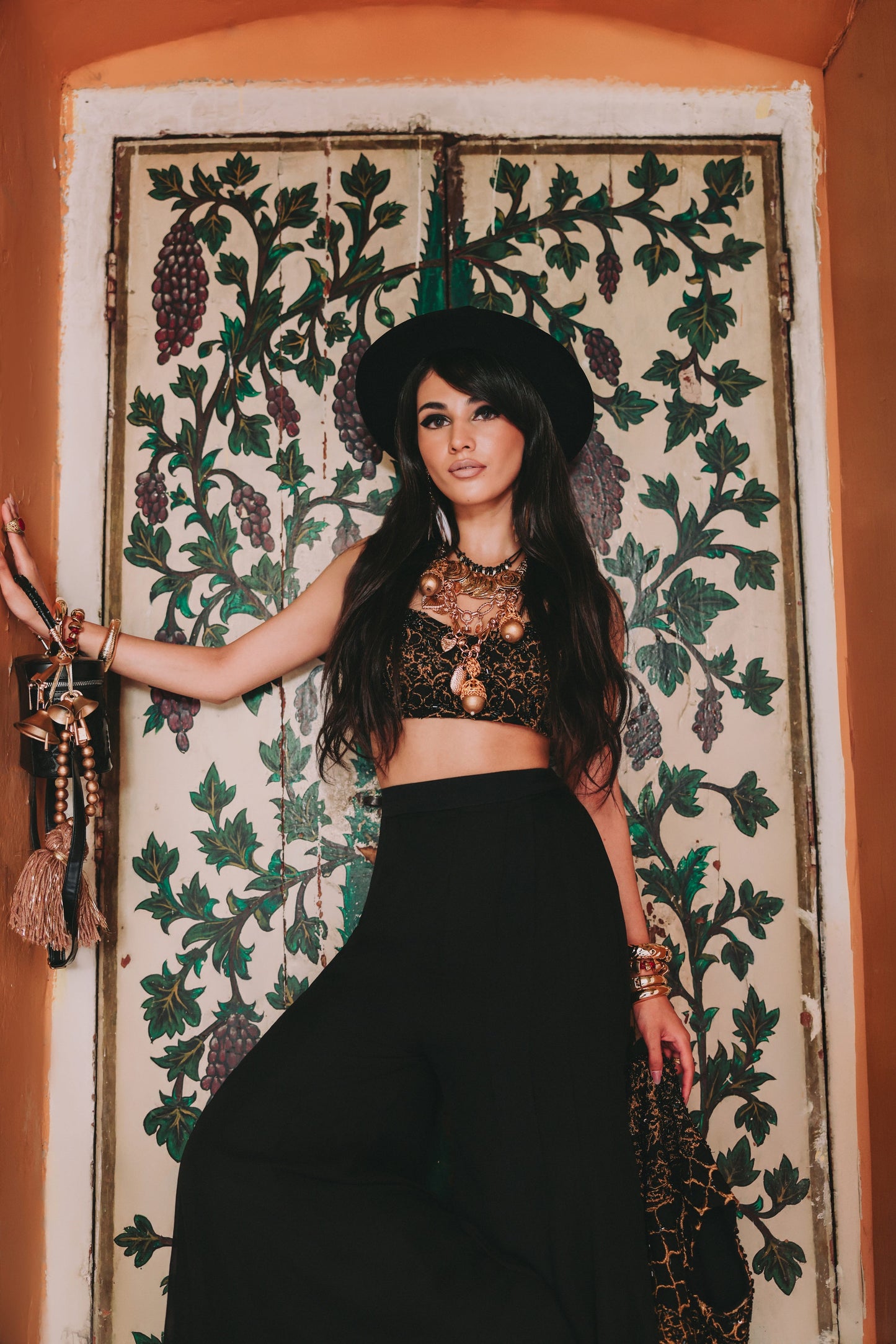 Woman in a black outfit with intricate patterns standing in front of a decorative wall.