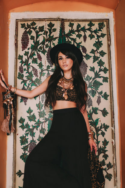 Woman in a black outfit with intricate patterns standing in front of a decorative wall.