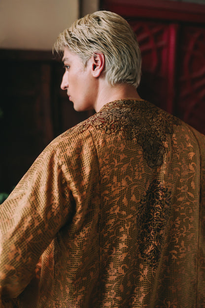 Person wearing a textured brown garment with intricate patterns.