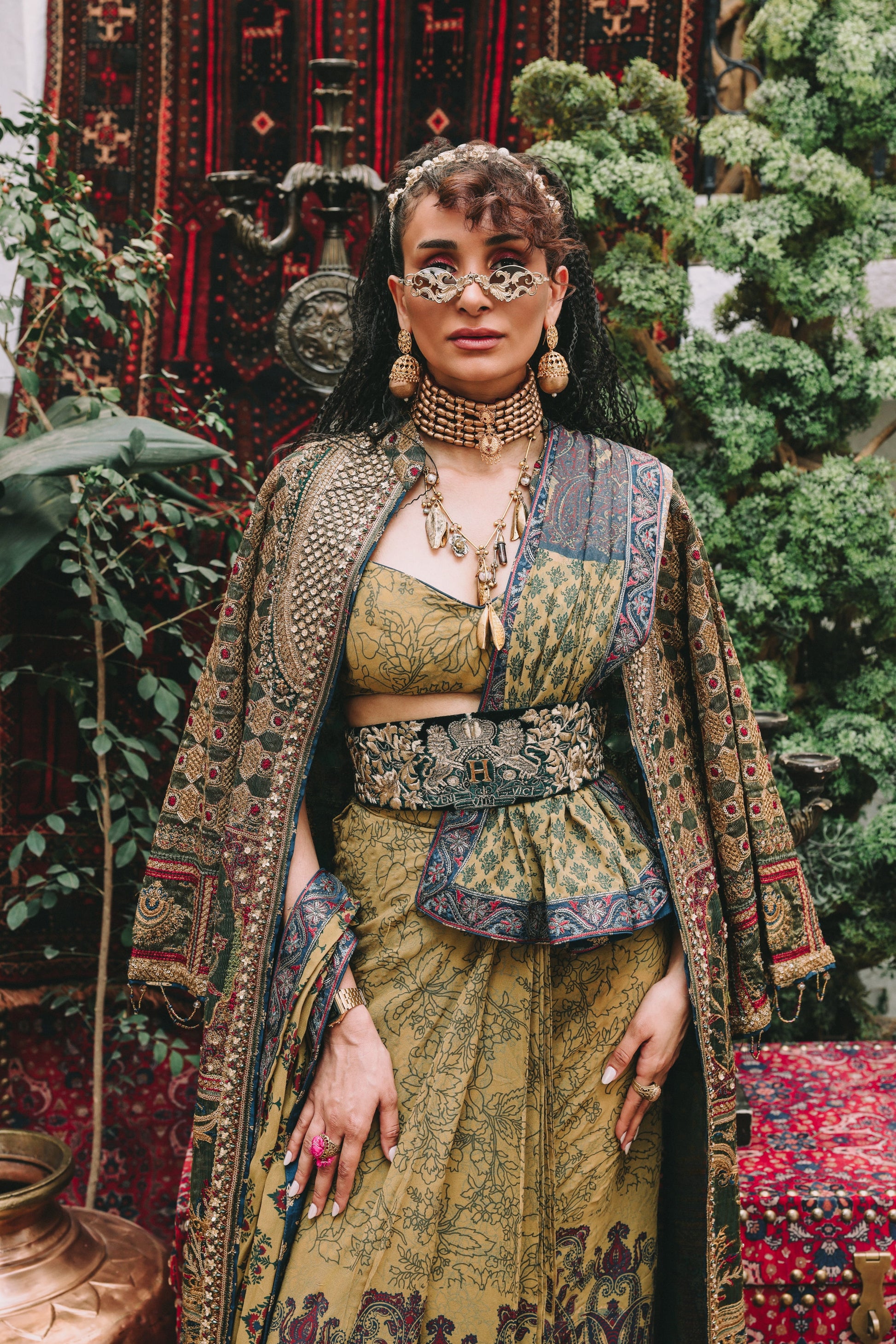 Woman in traditional attire with intricate patterns standing in a decorative setting.