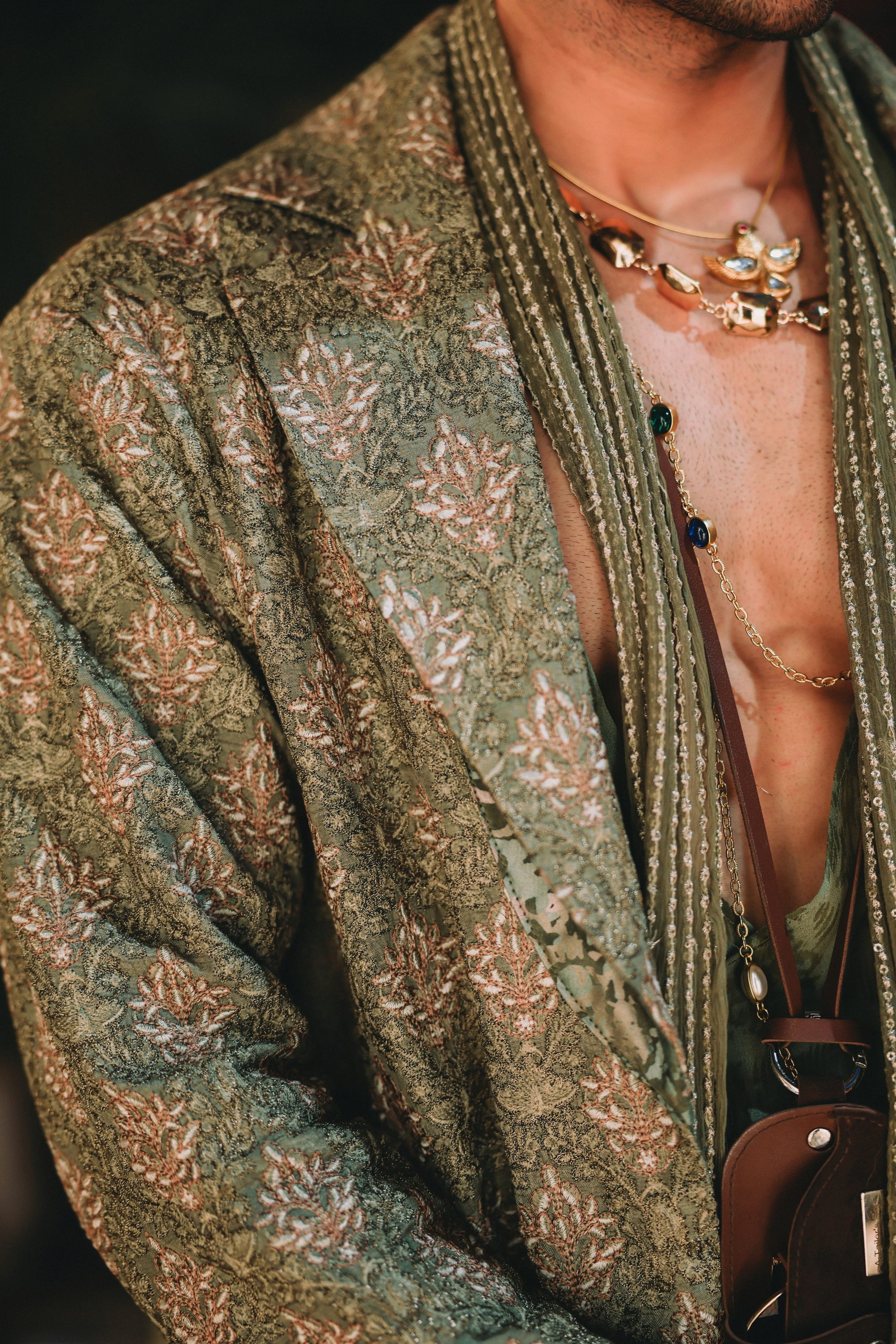 Person wearing a patterned green jacket with a necklace and a blurred background