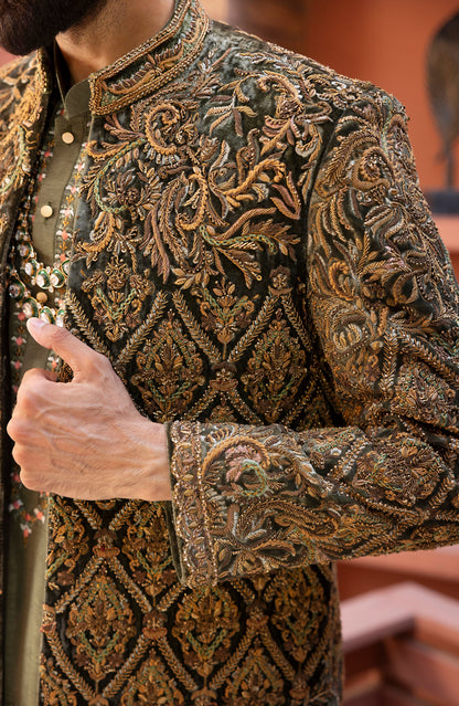 Close-up of a man wearing an ornate dark olive green sherwani jacket with intricate gold and brown embroidery, paired with a matching olive green shirt.