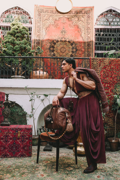 Man in traditional attire sitting on a chair with decorative rugs and patterns in the background