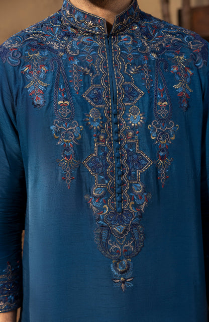 A close-up of a men's traditional kurta in a rich teal blue fabric, featuring intricate hand-embroidered patterns in gold, red, and blue along the front placket and shoulders.