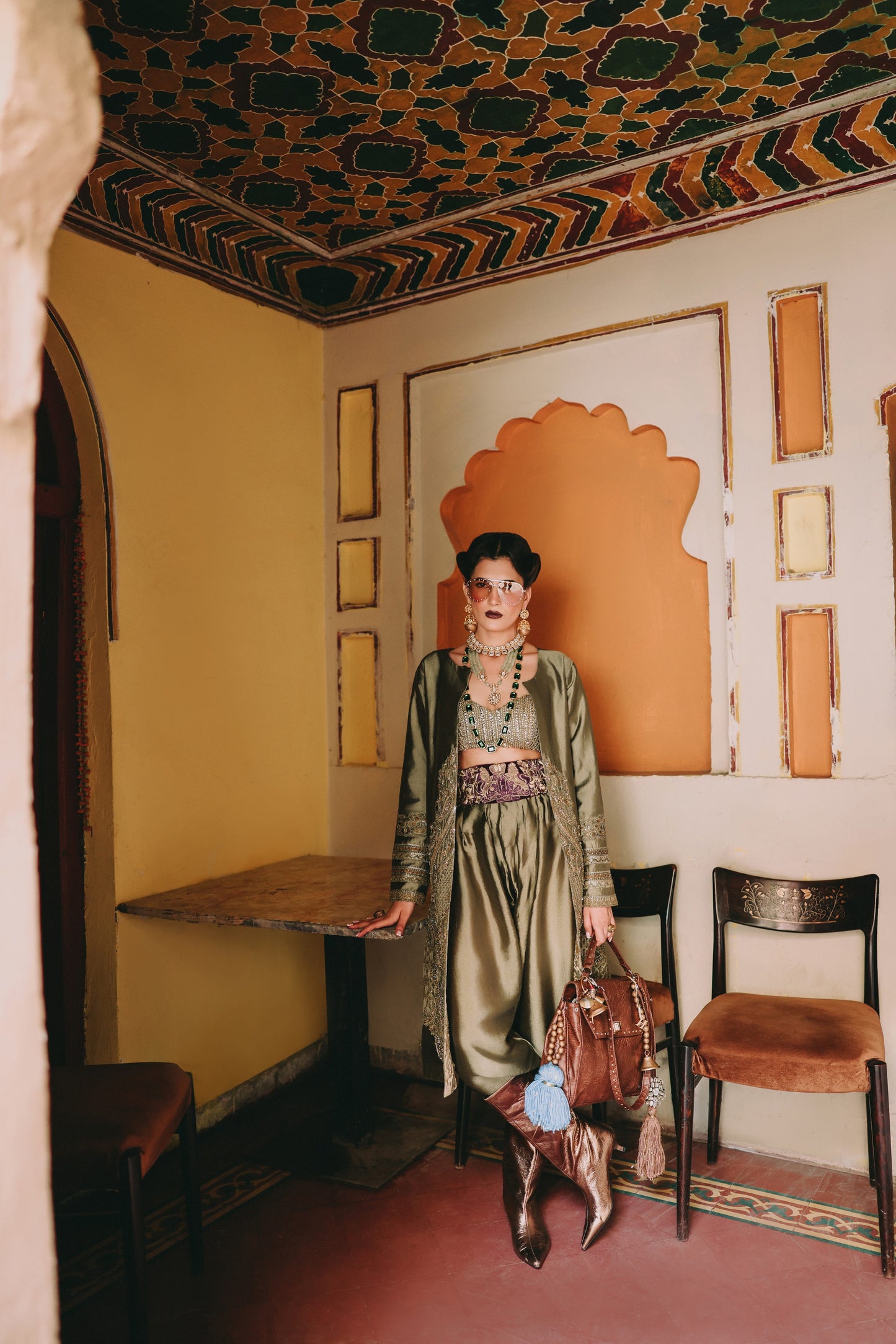 Woman in a green dress standing in a room with ornate decor and chairs.