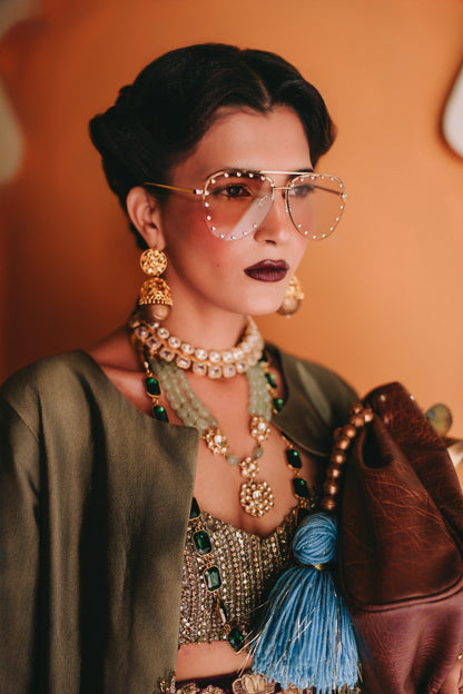 Woman wearing gold jewelry and sunglasses with a brown background