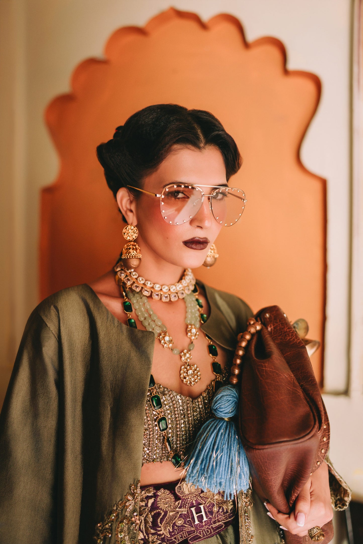 Woman in traditional outfit with jewelry and a handbag, standing in front of an ornate mirror.