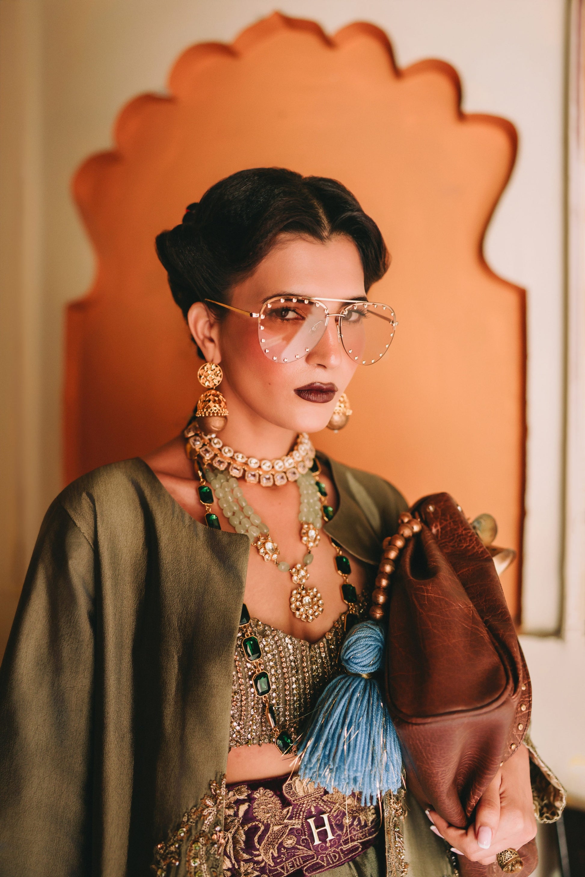 Woman in traditional outfit with jewelry and a handbag, standing in front of an ornate mirror.