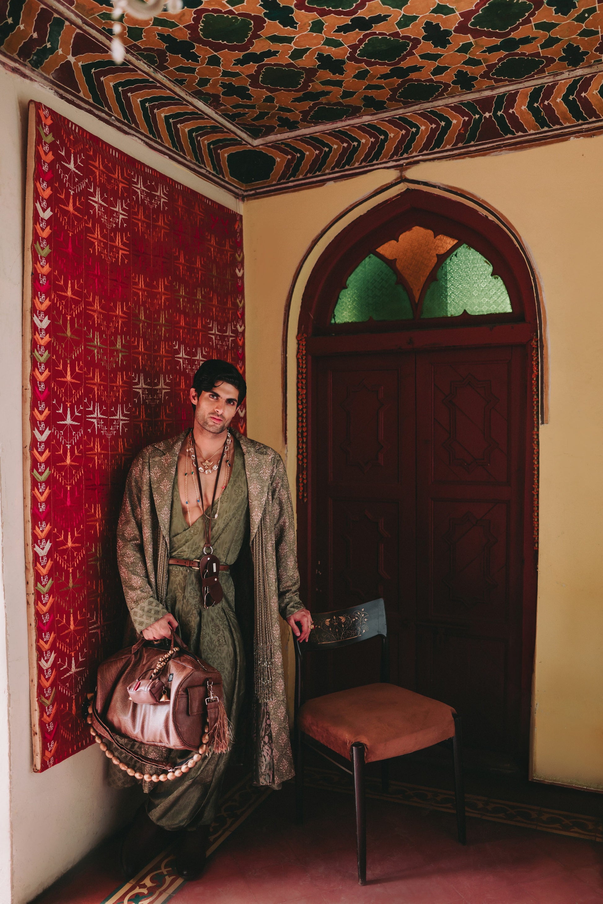 Person in traditional attire standing in a room with ornate ceiling and wall decorations.