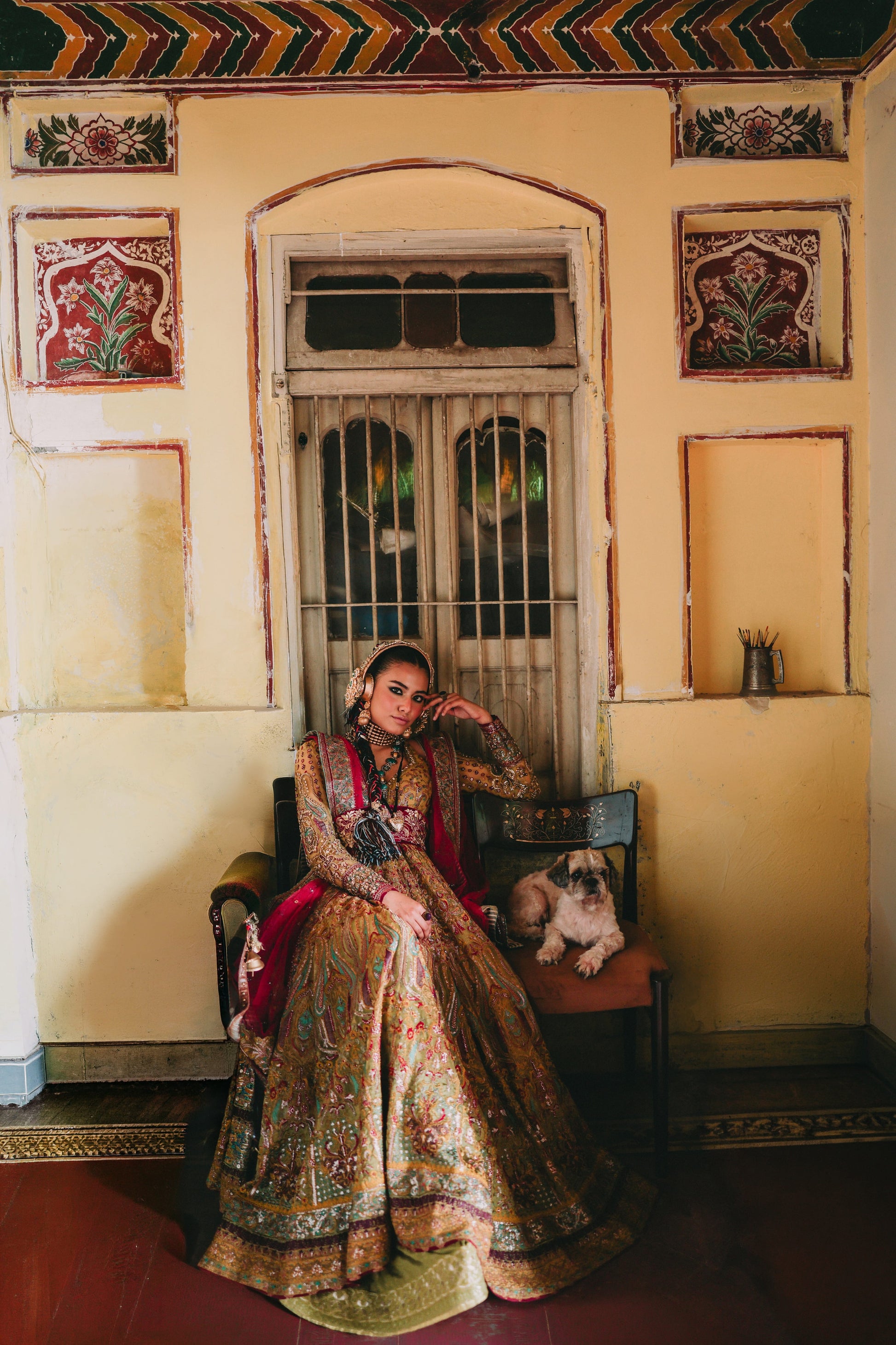Woman in traditional attire sitting on a chair with a dog in a decorated room.
