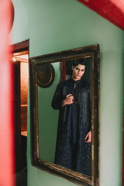 Person in a dark outfit standing in front of a mirror with a green wall and red frame.