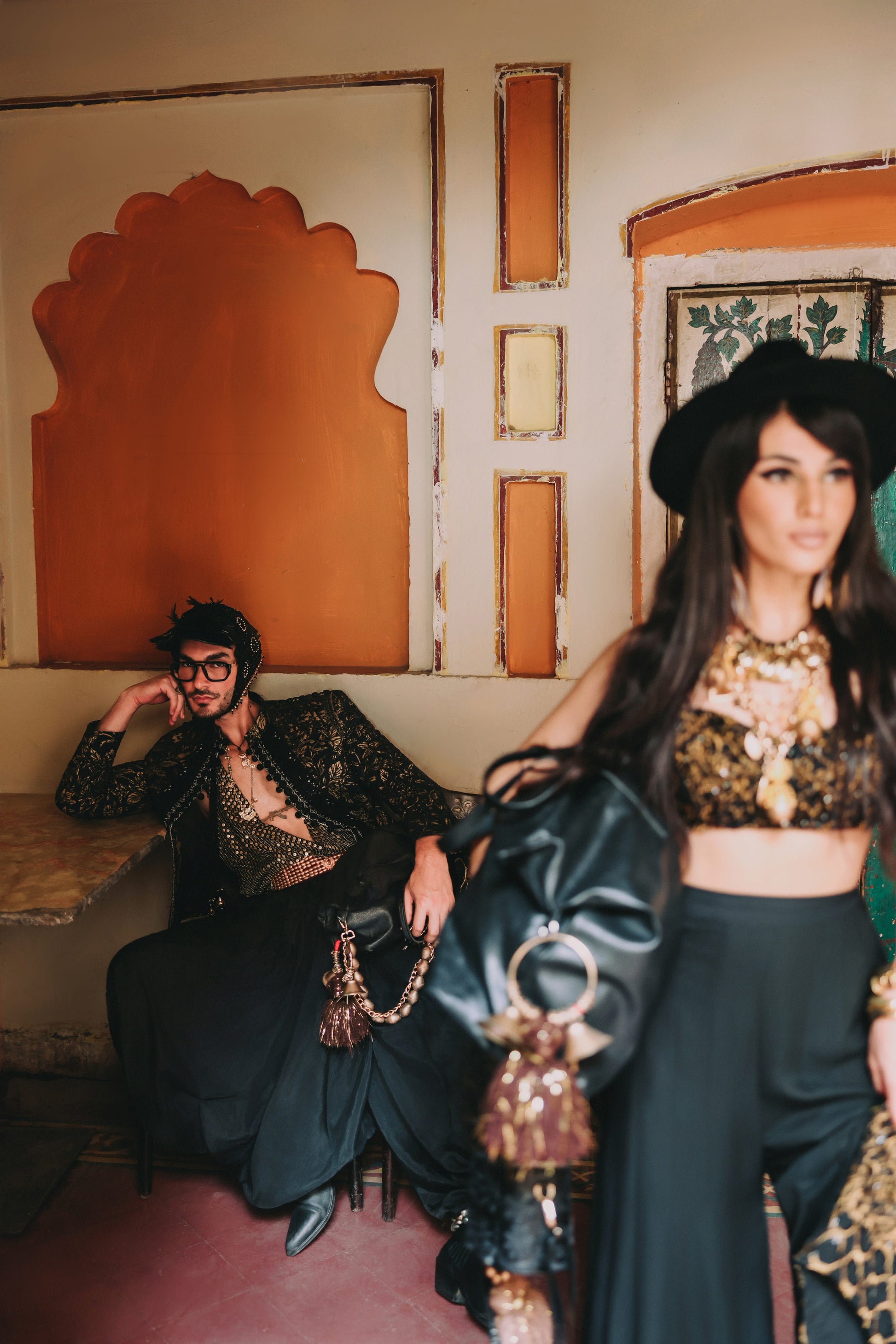 Two people in stylish outfits in a decorative interior setting.