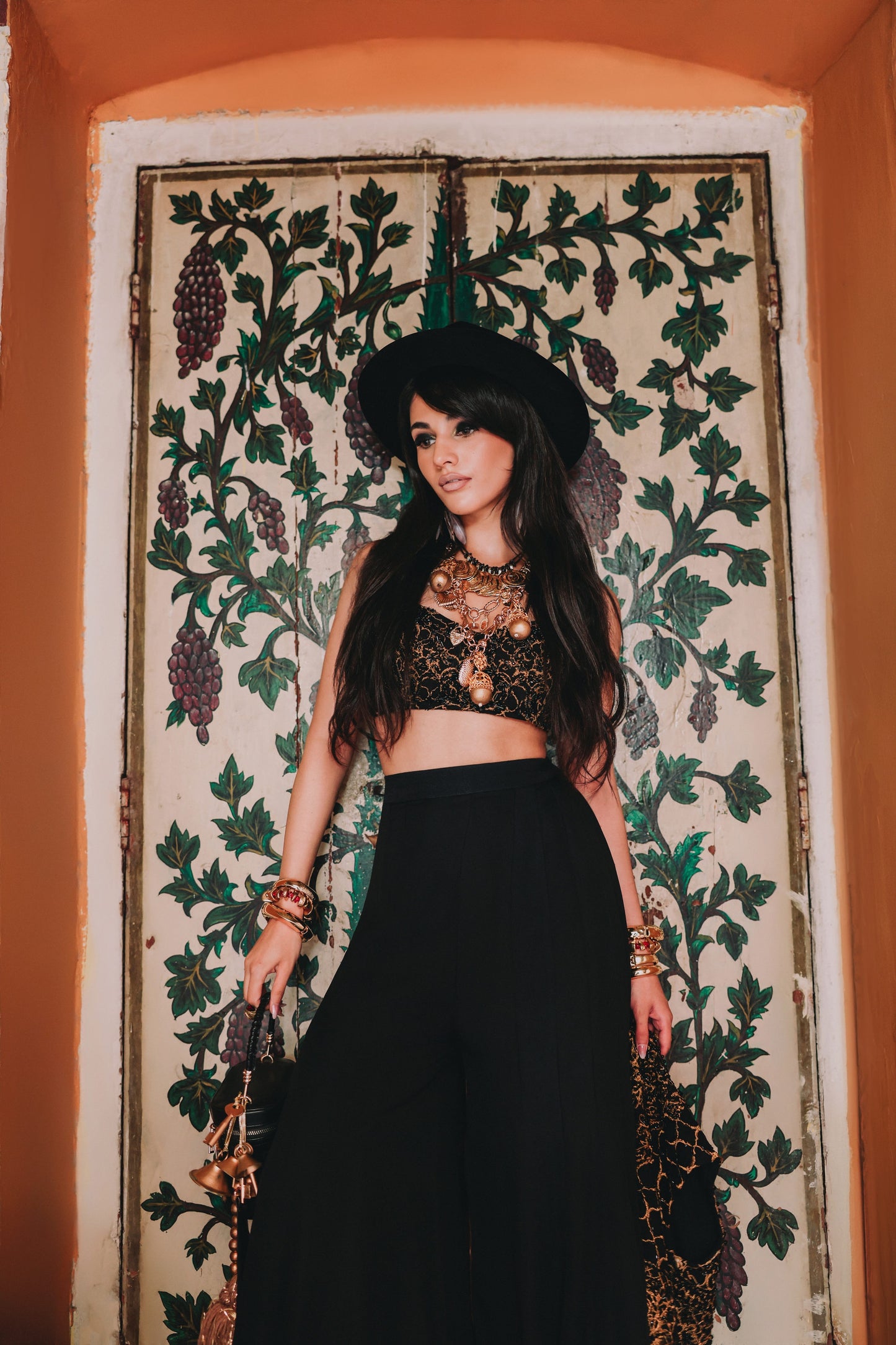 Woman in a black outfit with gold accents standing in front of an ornate wall.