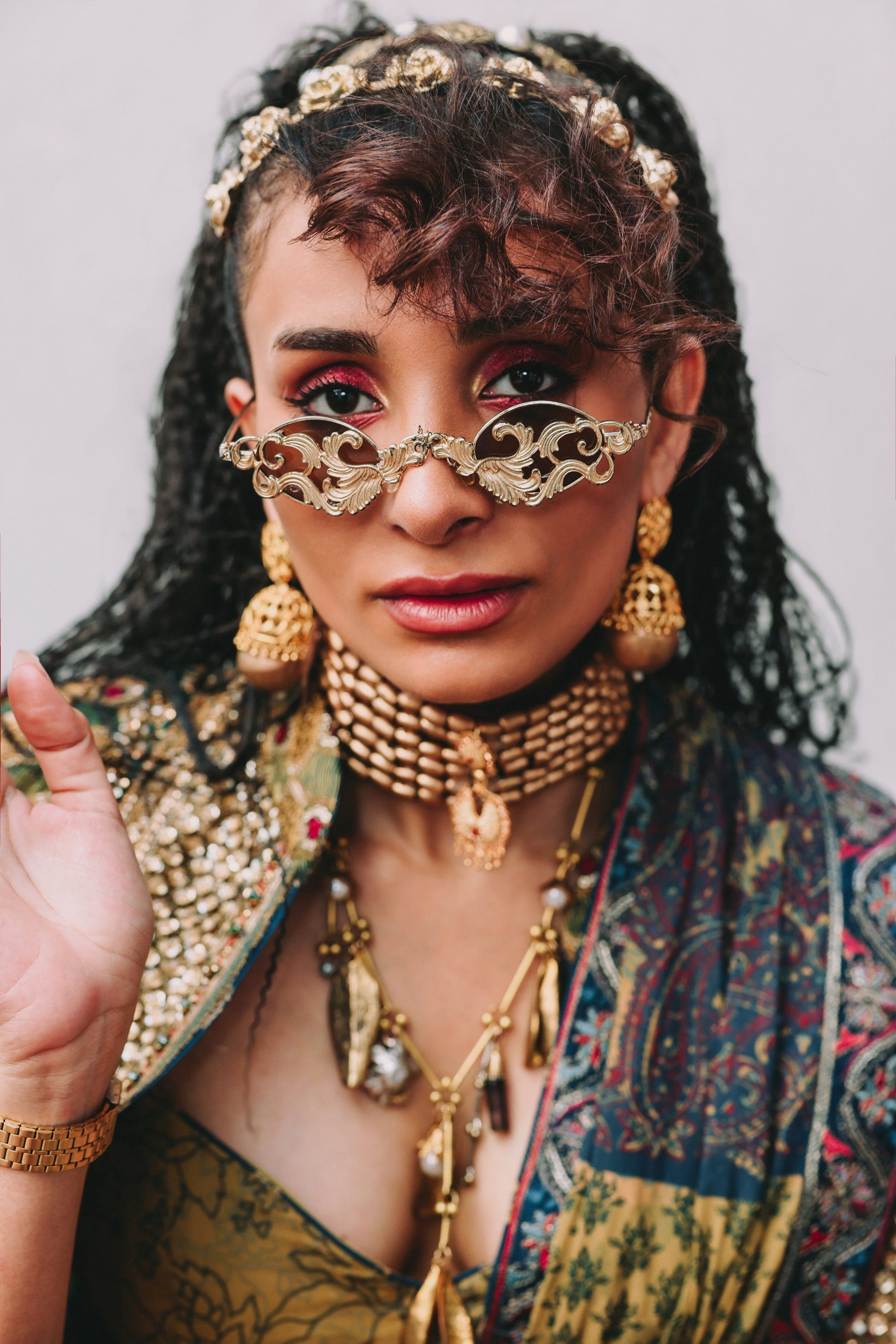 Woman wearing elaborate gold jewelry and traditional attire against a neutral background