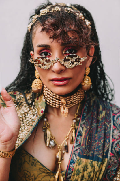 Woman wearing elaborate gold jewelry and traditional attire against a neutral background