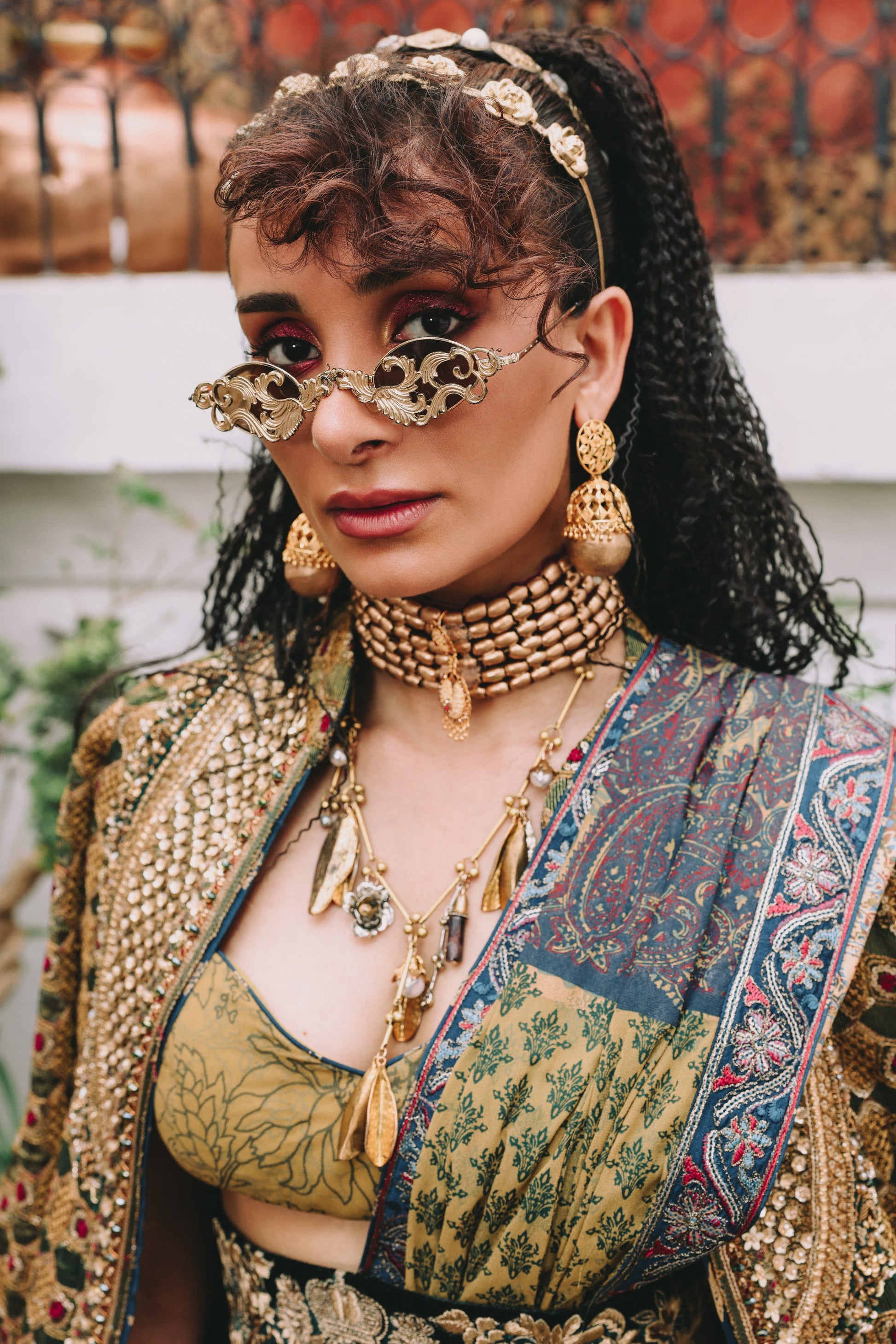 Woman wearing elaborate jewelry and traditional outfit with a patterned background