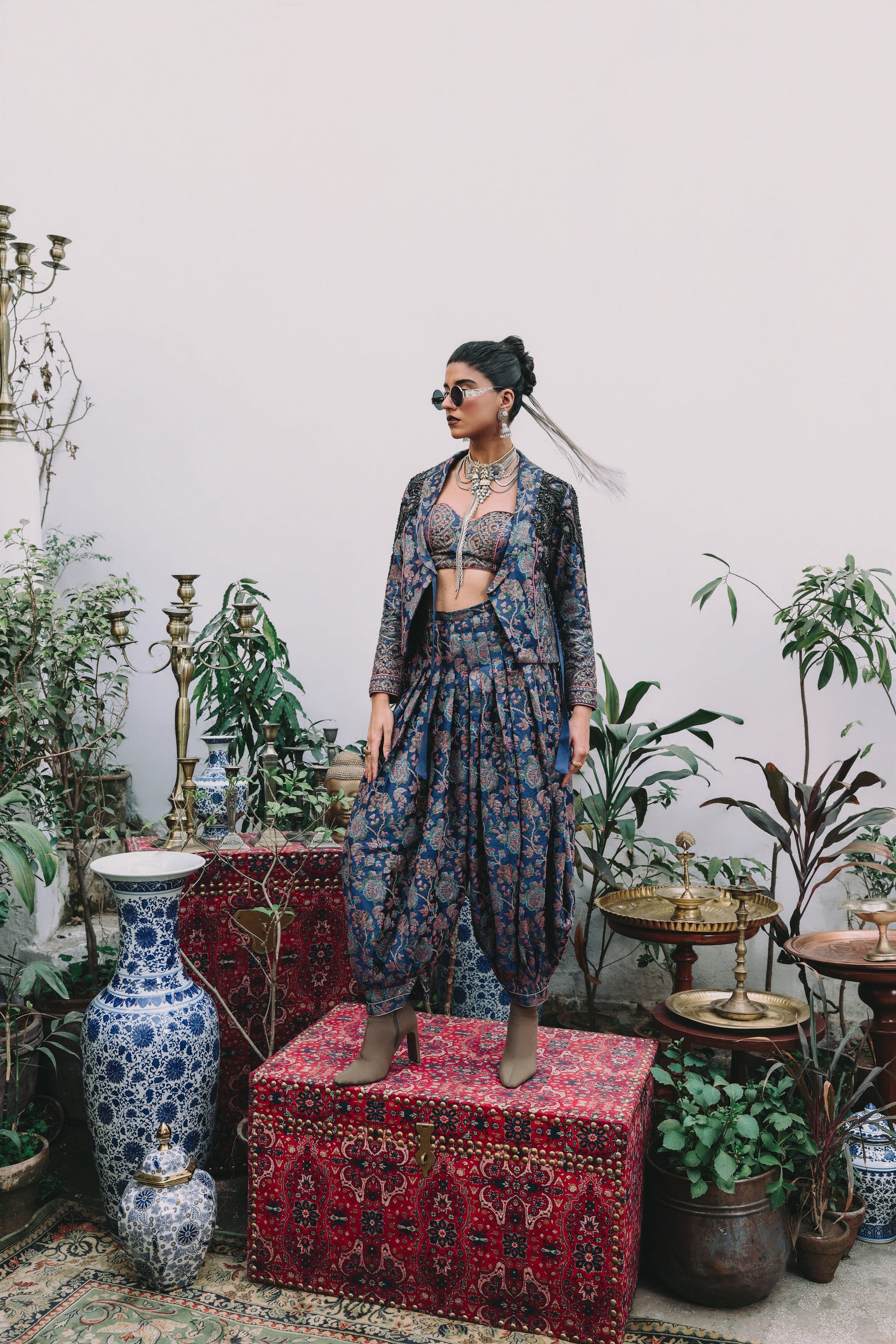 Woman in a patterned outfit standing in a room with plants and decorative items.