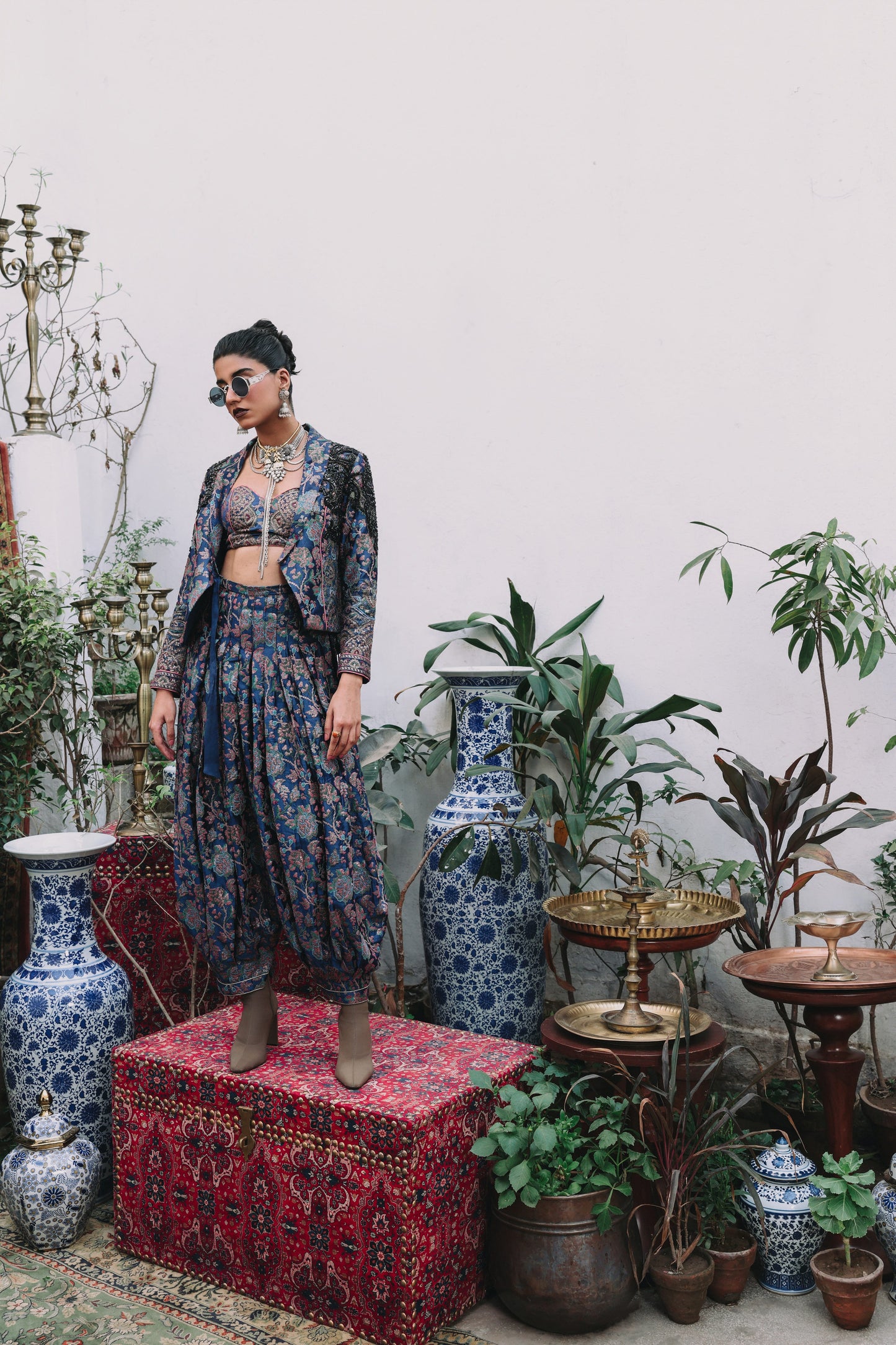 Woman in a floral outfit standing in a room with decorative vases and plants.
