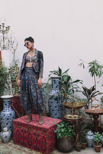 Woman in a floral outfit standing in a room with decorative vases and plants.