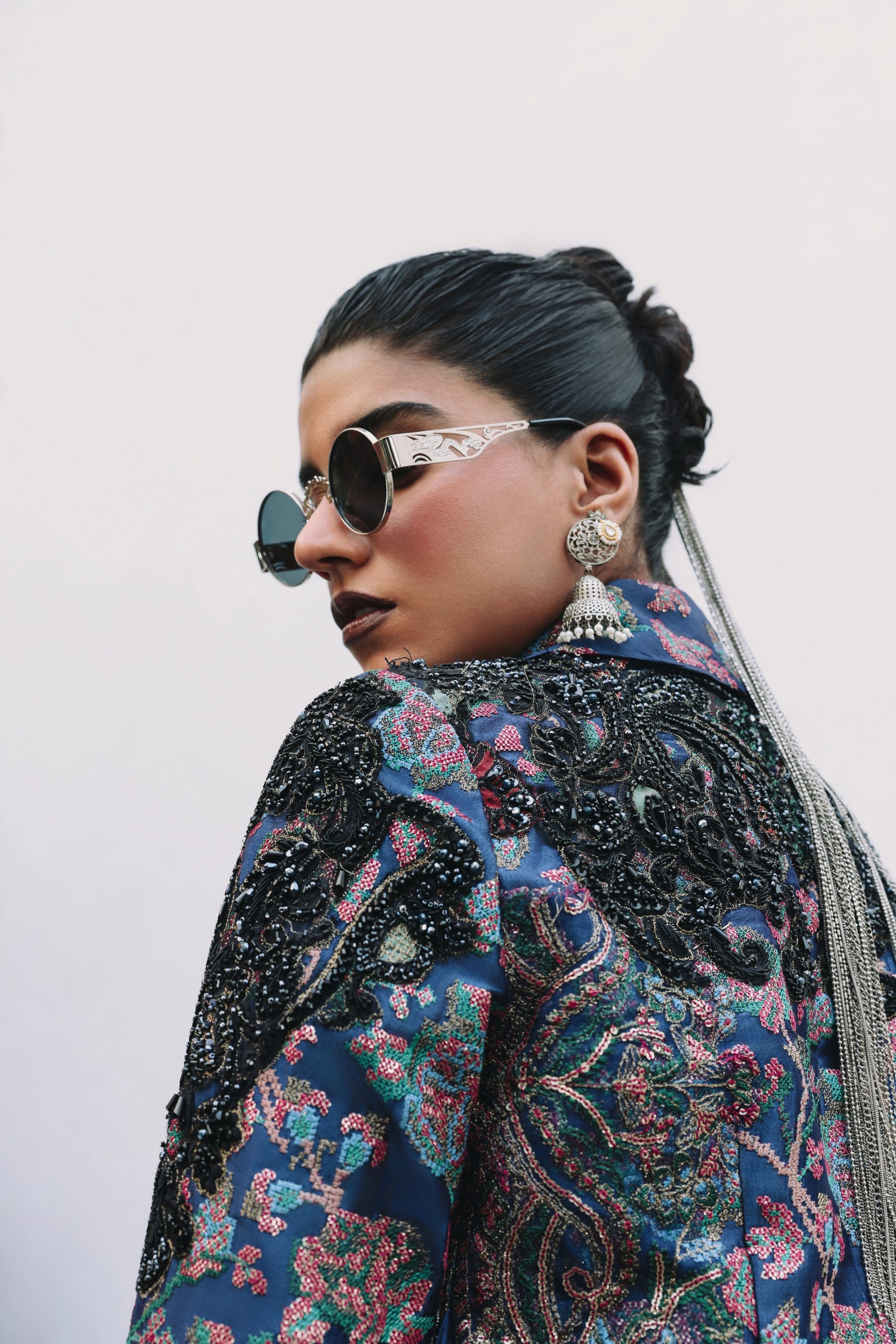 Person wearing a patterned jacket with intricate designs and sunglasses.