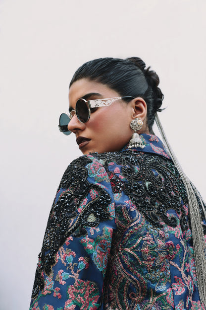 Person wearing a patterned jacket with intricate designs and sunglasses.