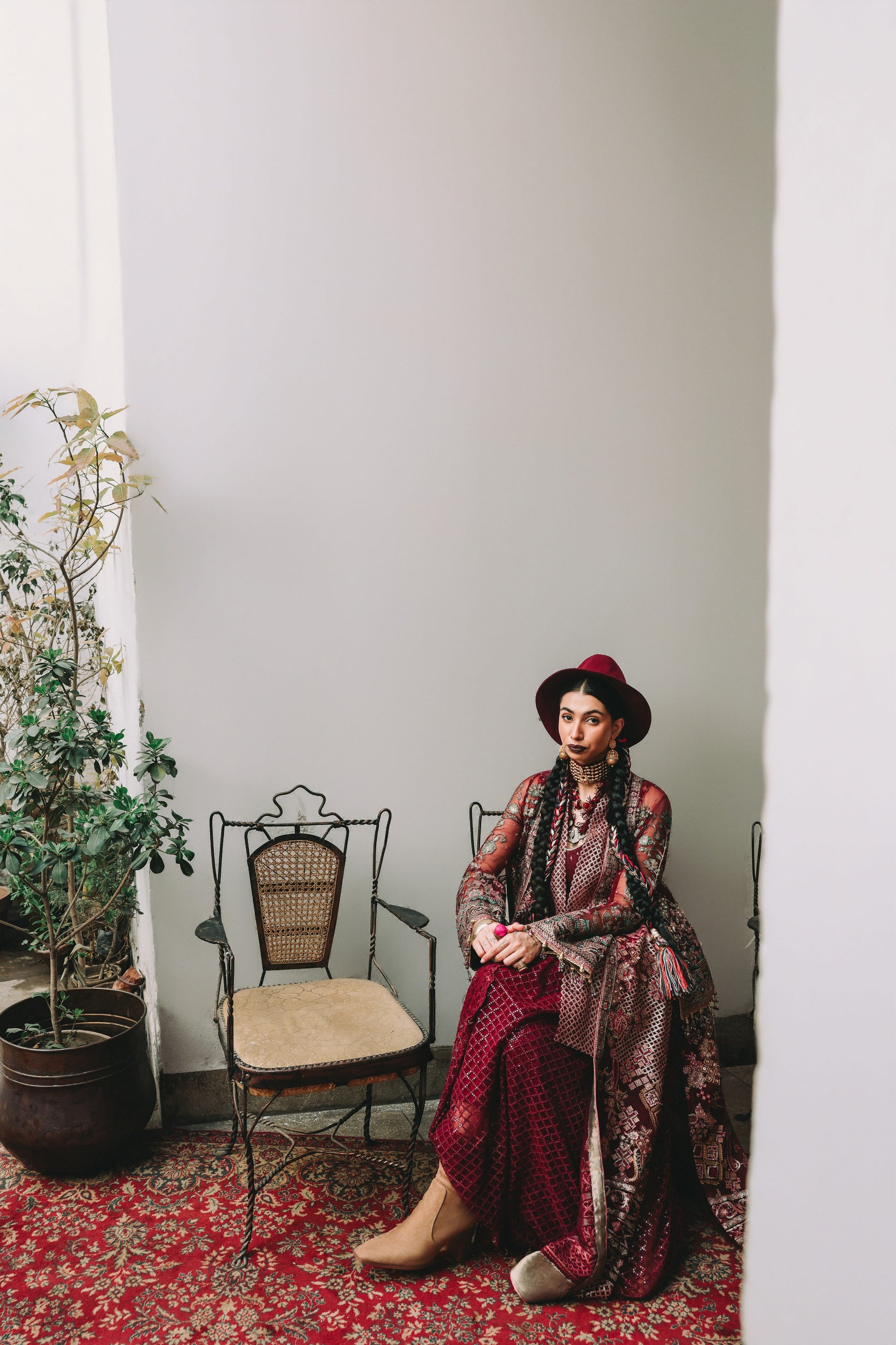 Woman in a patterned dress sitting on a chair in a room with a plant and rug.
