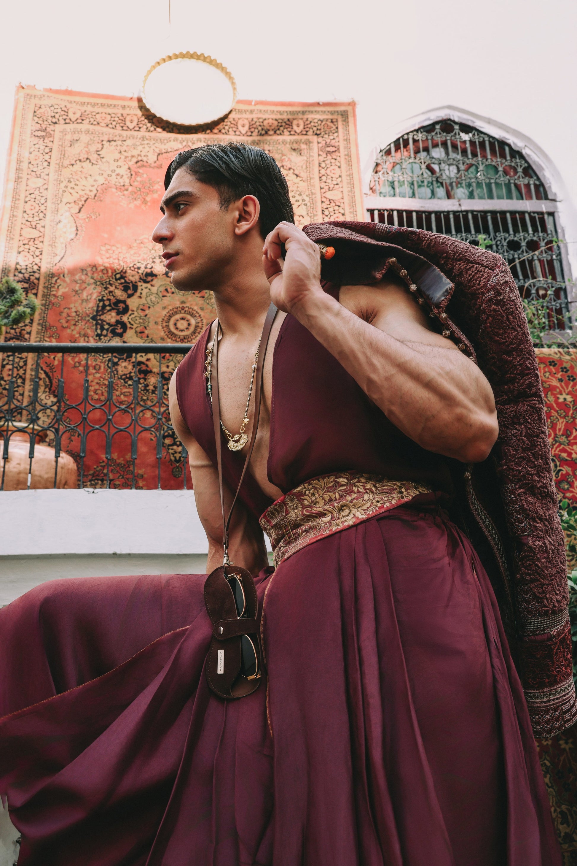 Person in a burgundy dress with intricate patterns, standing against a decorative wall.