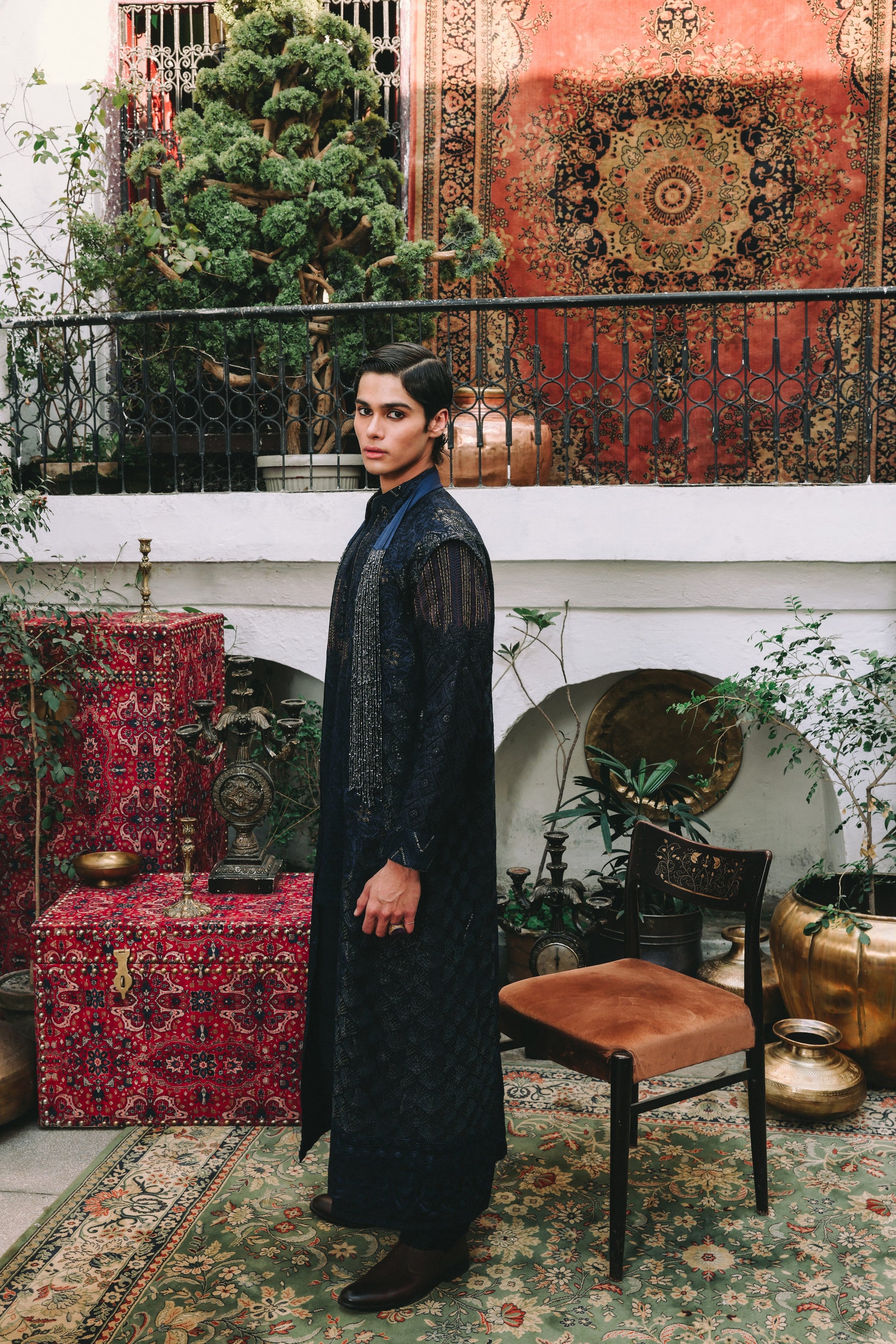 Person in a black outfit standing in an ornate room with patterned rugs and furniture.