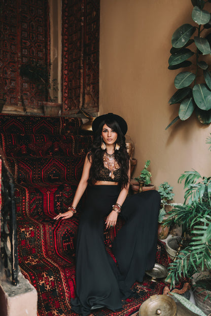 Woman in a black outfit sitting on a patterned rug with plants around
