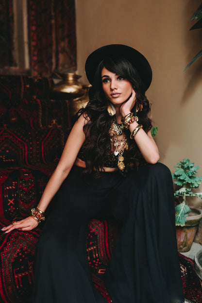 Woman in a black outfit with jewelry sitting on a patterned chair.