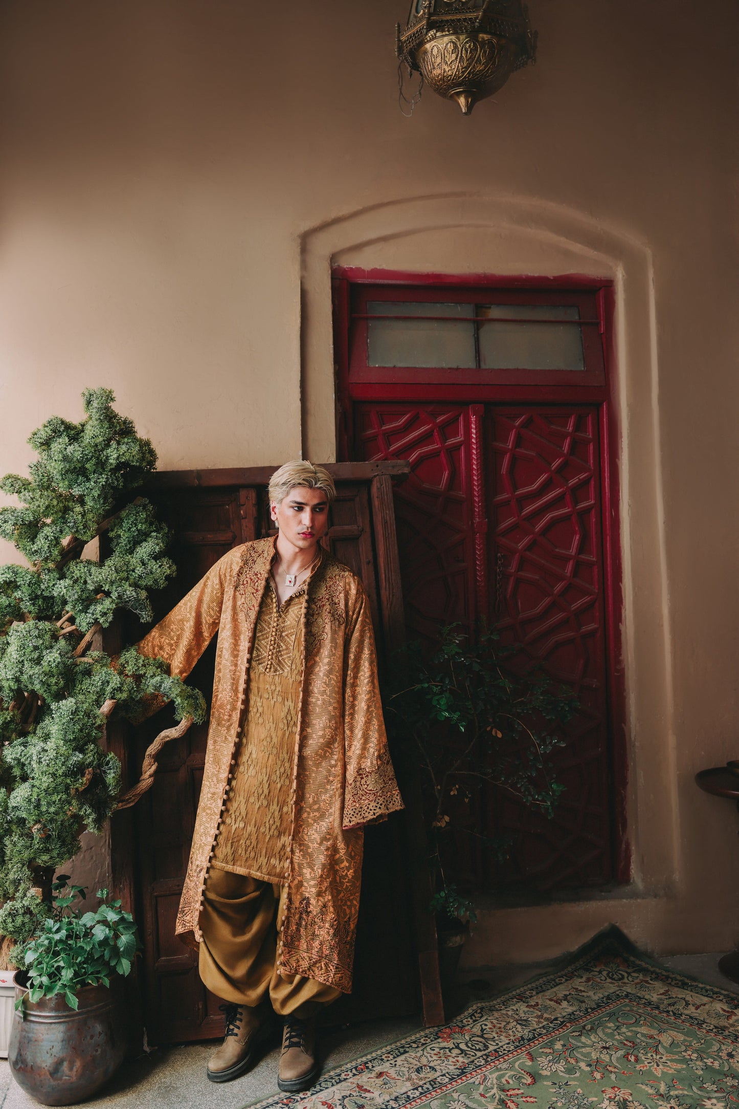 Person in traditional attire standing in a room with a red door and plants.