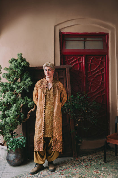 Person wearing a patterned outfit standing in a room with a red door and plants.