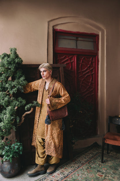 Man in a long, patterned coat standing in a room with a red door and plants.