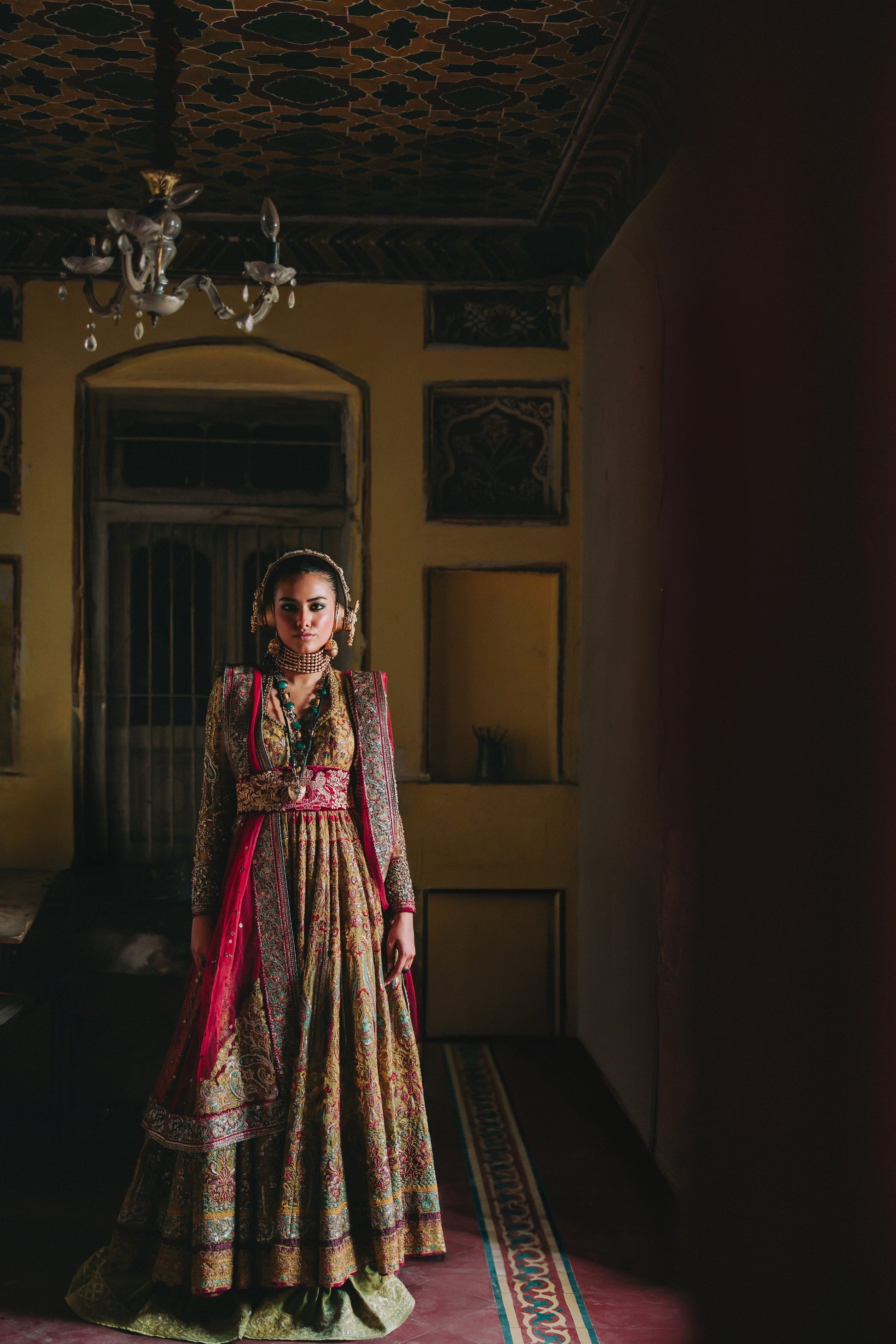 Woman in traditional attire standing in a dimly lit room with ornate ceiling.